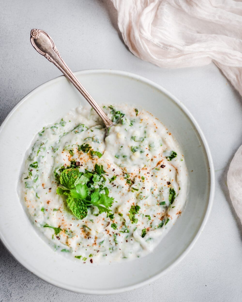 vegan raita in a white bowl with spoon. 