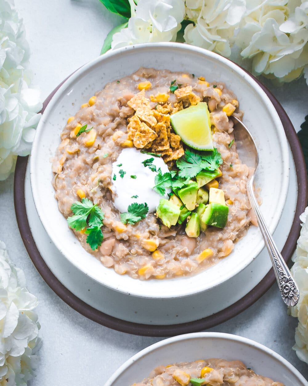 White bean chili with toppings in a white bowl on a table next to flowers.