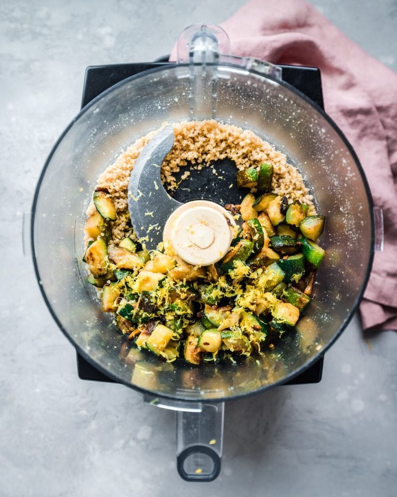 Jammy zucchini and lemon zest being added to food processor with basil and pine nuts