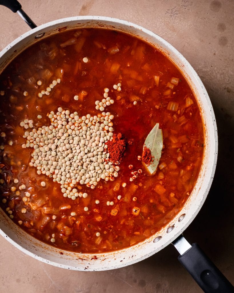 pouring in vegetable broth, lentils, paprika, and bay leaf