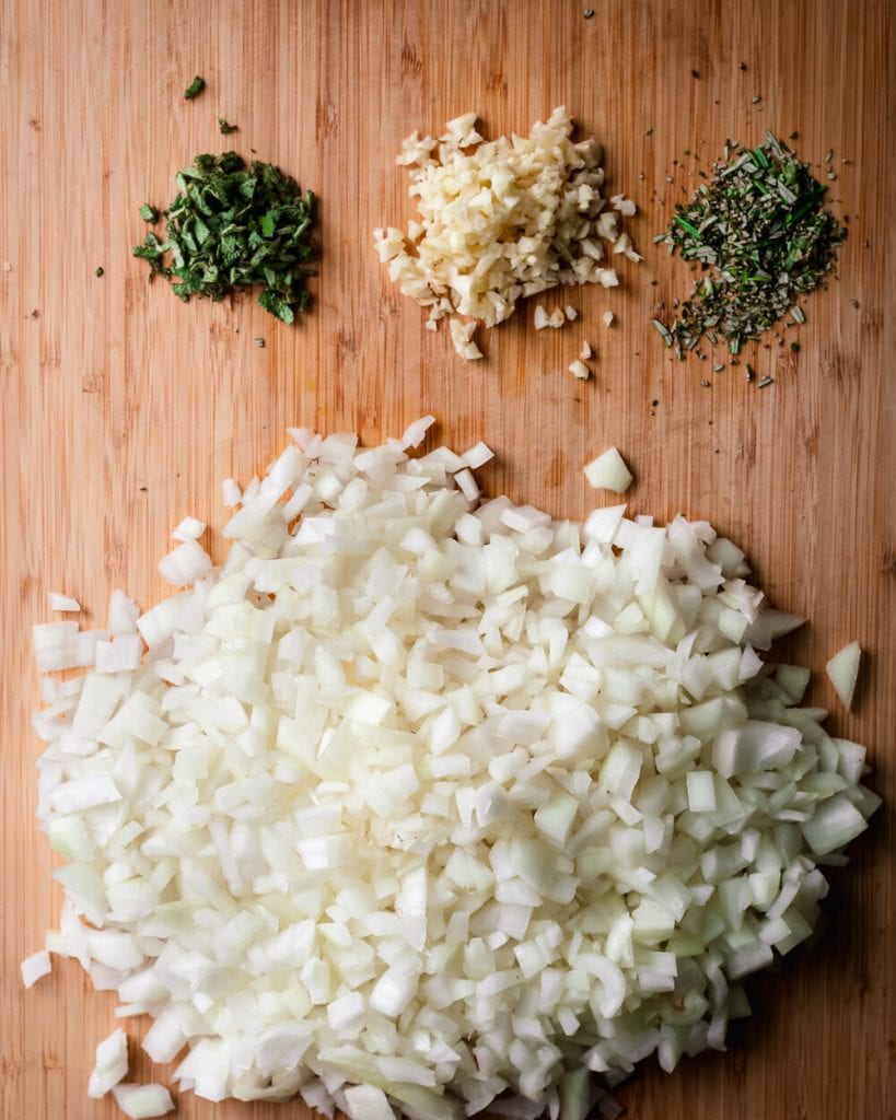 raw onion, garlic, rosemary and sage on cutting board