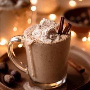 creamy vegan spiced eggnog in glass mug with holiday lights