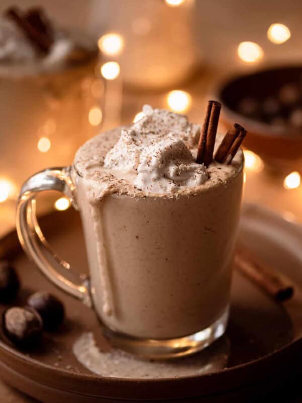 creamy vegan spiced eggnog in glass mug with holiday lights