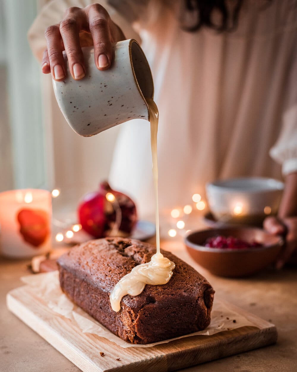 Woman pouring icing onto gingerbread cake on wood cutting board.