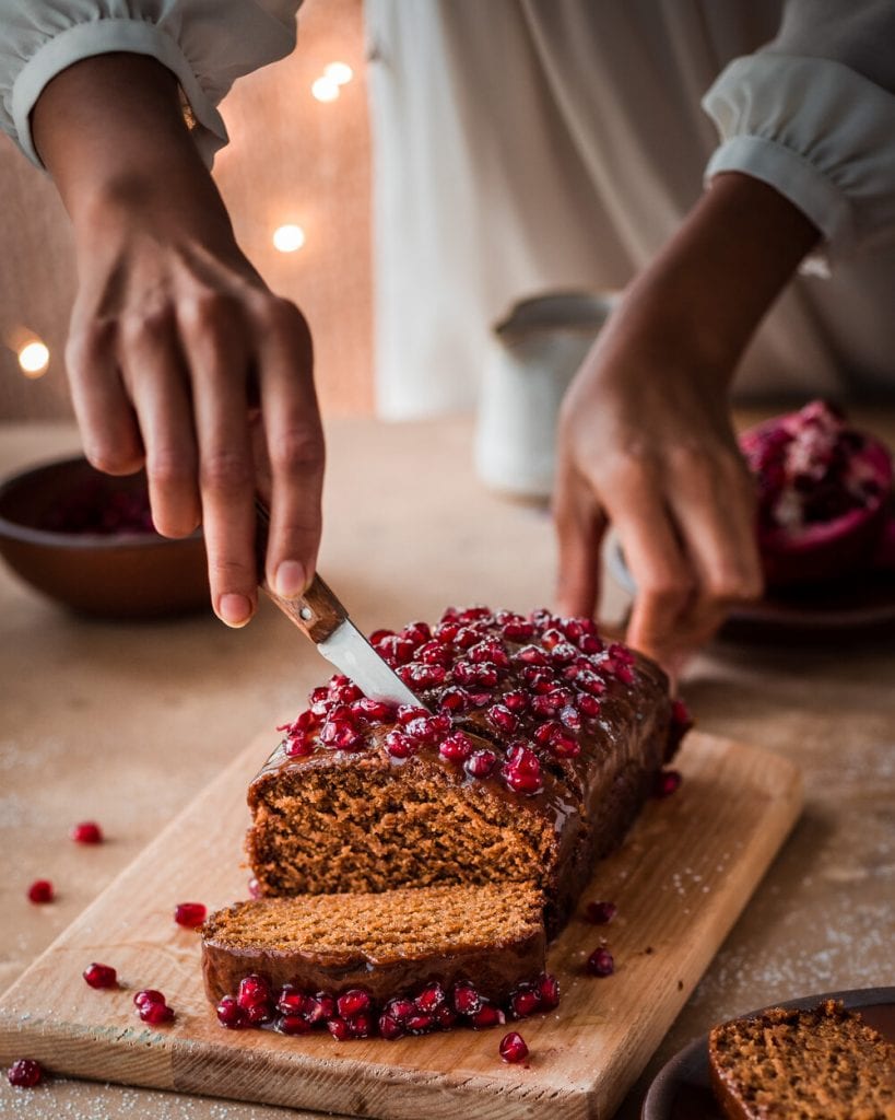 woman slicing gingerbread cake with pomegranate seeds with holiday scene