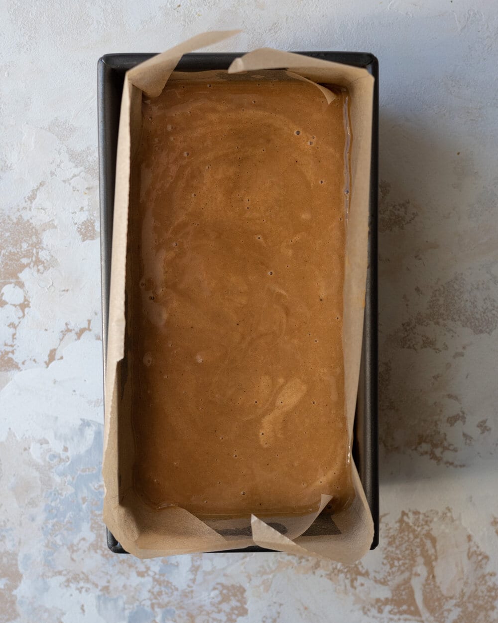 Cake batter in a loaf pan lined with parchment paper.