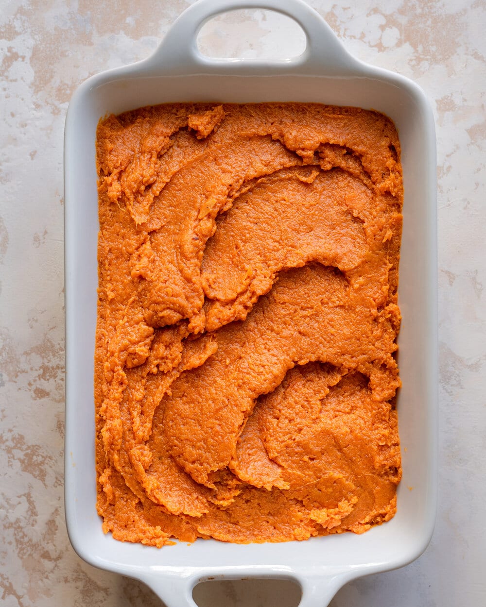 Seasoned mashed sweet potatoes after being smoothed out in a casserole dish.