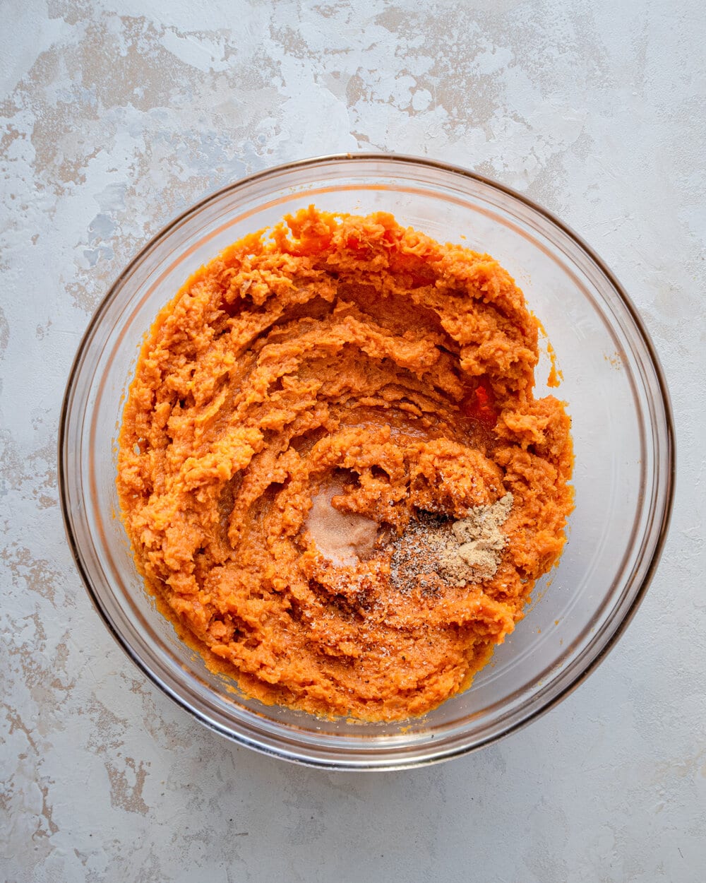Spices on top of mashed sweet potatoes in a glass bowl.