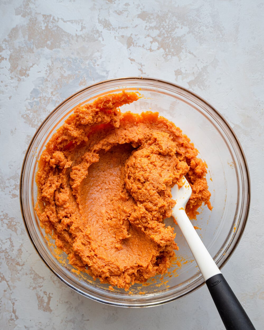 Mashed sweet potatoes mixed with spices in a glass bowl.