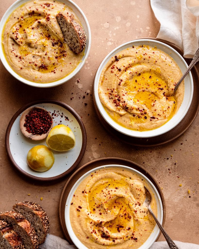 3 bowls of creamy cauliflower white bean soup garnished with olive oil and lemon