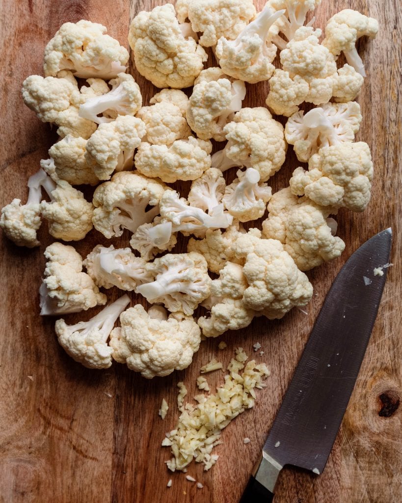 cauliflower florets and chopped garlic on cutting board