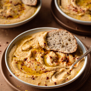 bowl of creamy vegan cauliflower soup with spoon dug in and bread dipped in on a brown table with two bowls in back.