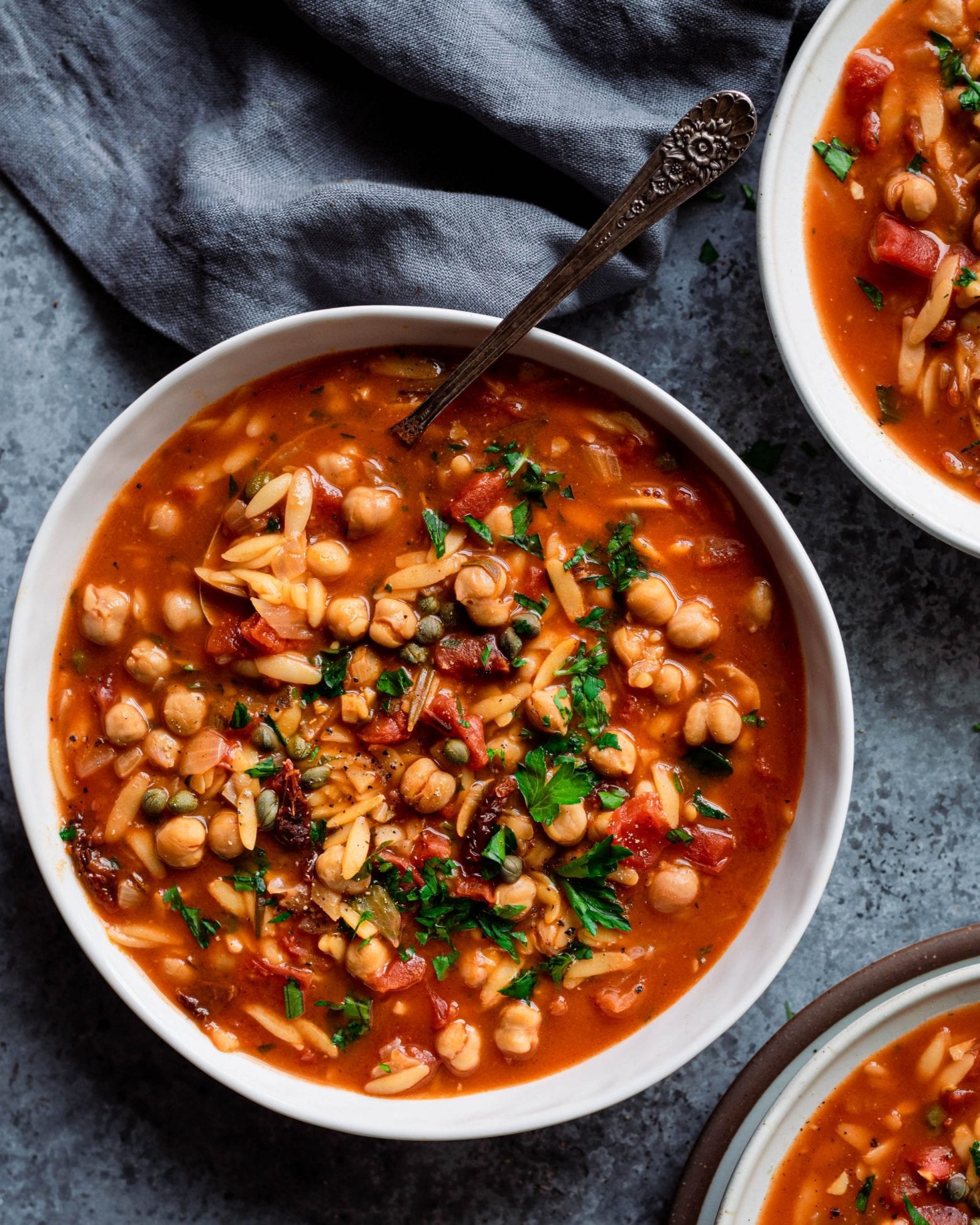 bowl of chickpea orzo soup on blue background with napkin