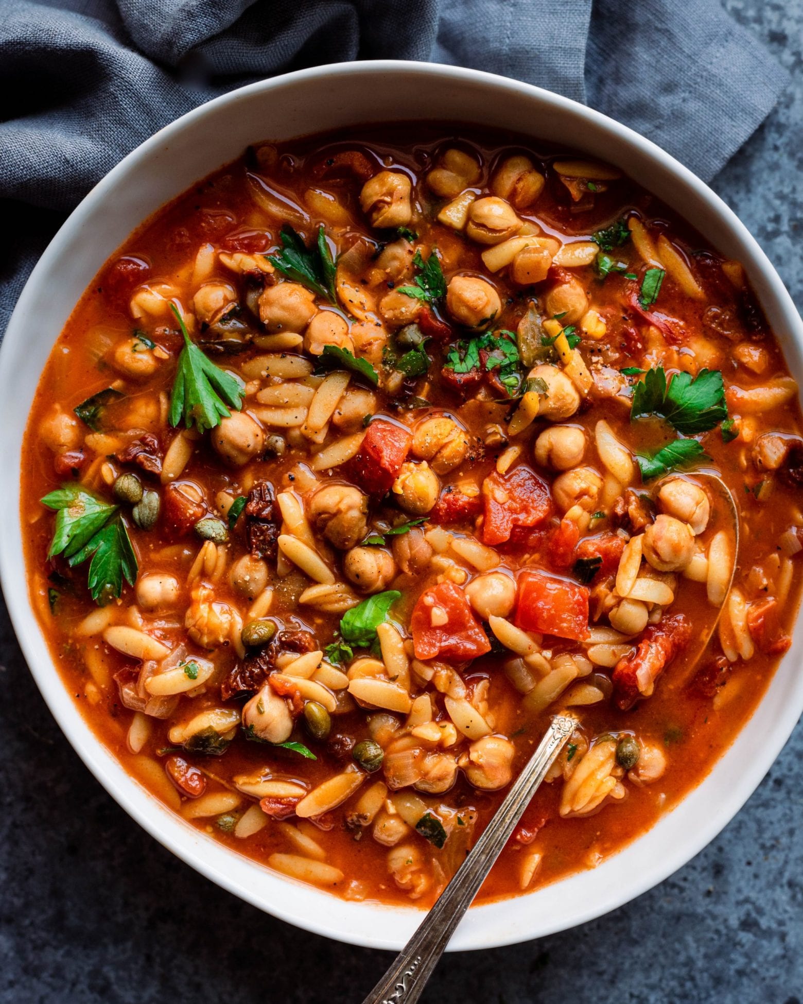 Bowl of chickpea orzo soup with a spoon in it.