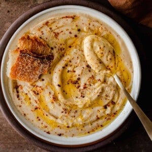 bowl of creamy vegan cauliflower soup in a white bowl with spoon and bread in soup.