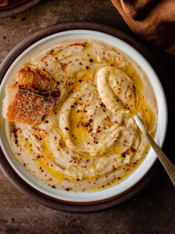 bowl of creamy vegan cauliflower soup in a white bowl with spoon and bread in soup.