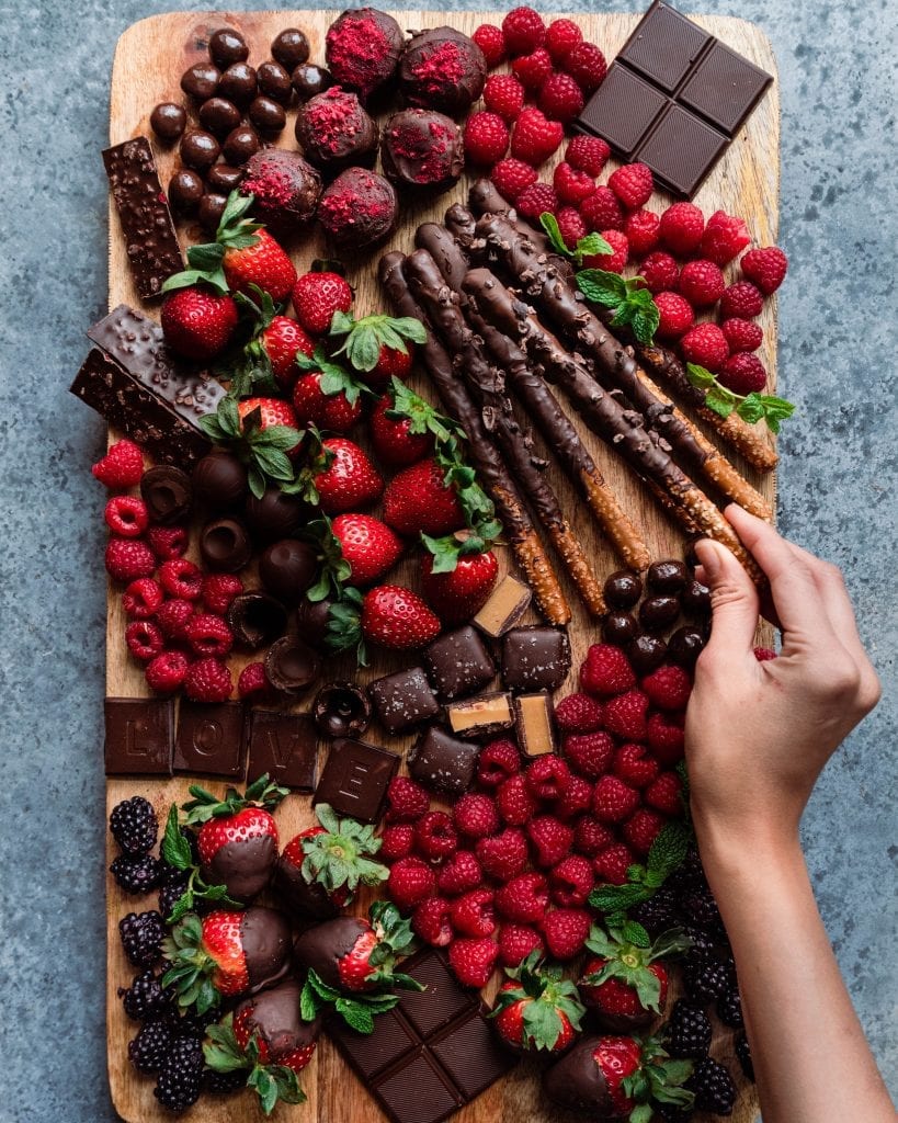 hand reaching for chocolate covered pretzel on dessert charcuterie board