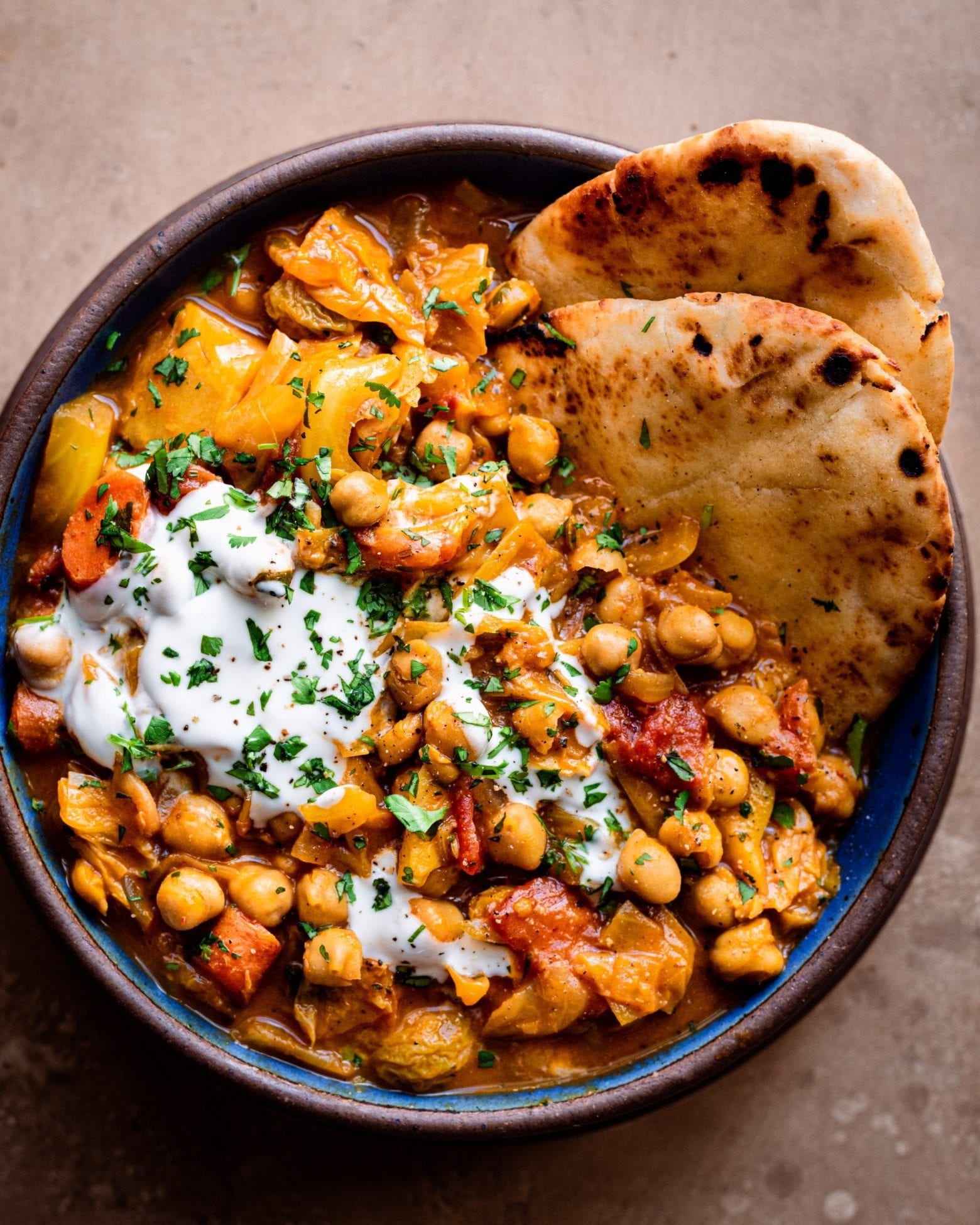 braised chickpea stew and naan in a blue and brown bowl on brown countertop