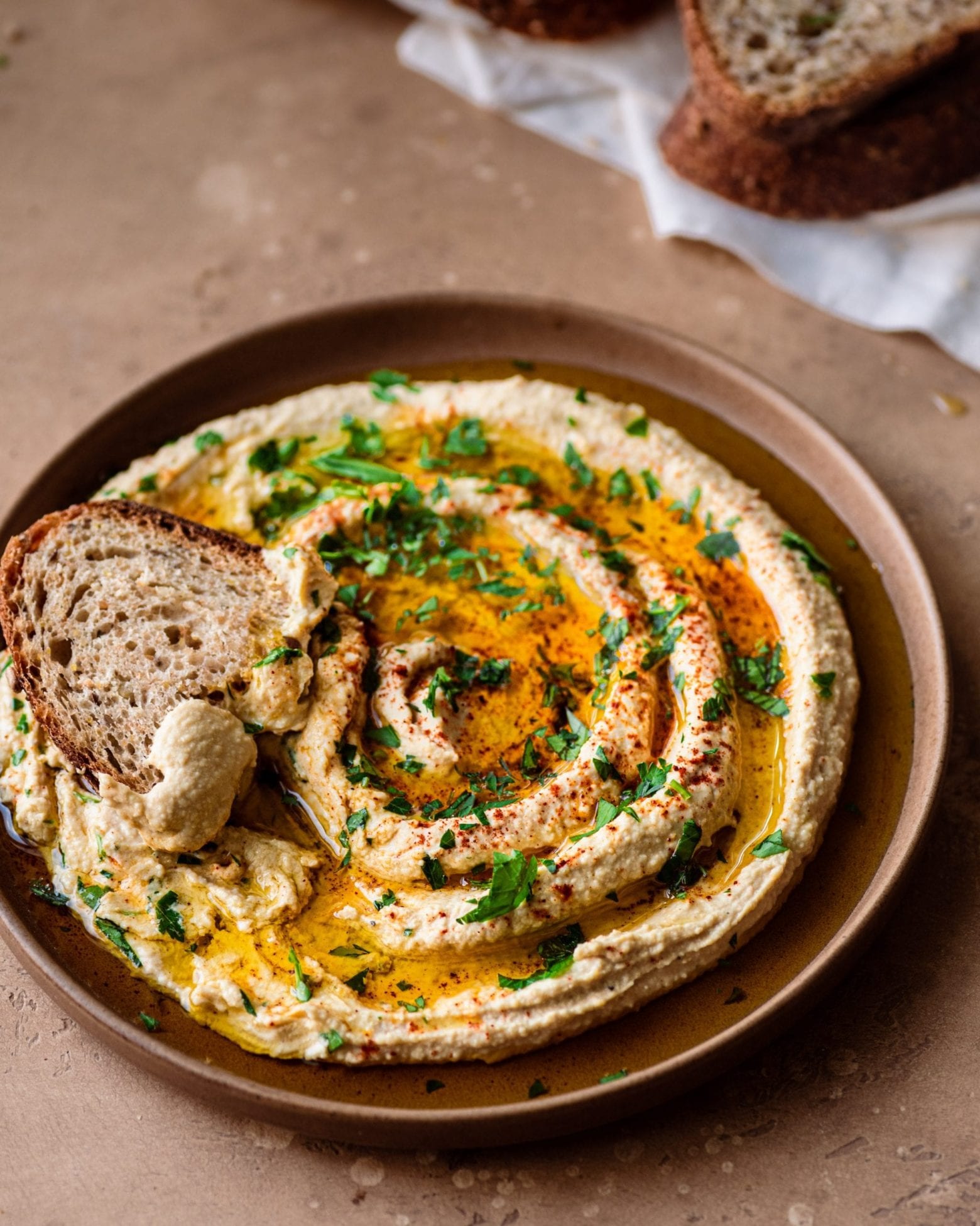 plate of swirled hummus with olive oil and parsley, and hunk of bread dipped in