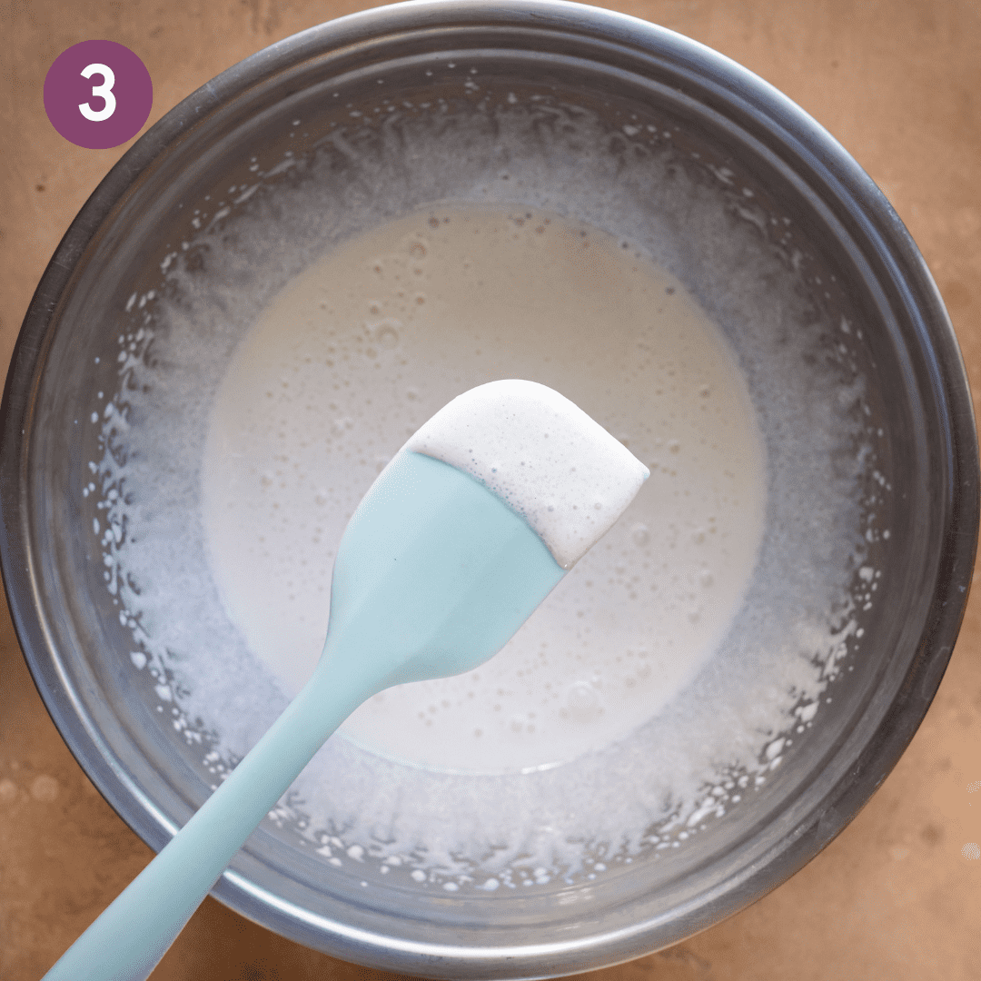 blue silicone spatula with whipped aquafaba above a mixing bowl to show the texture.