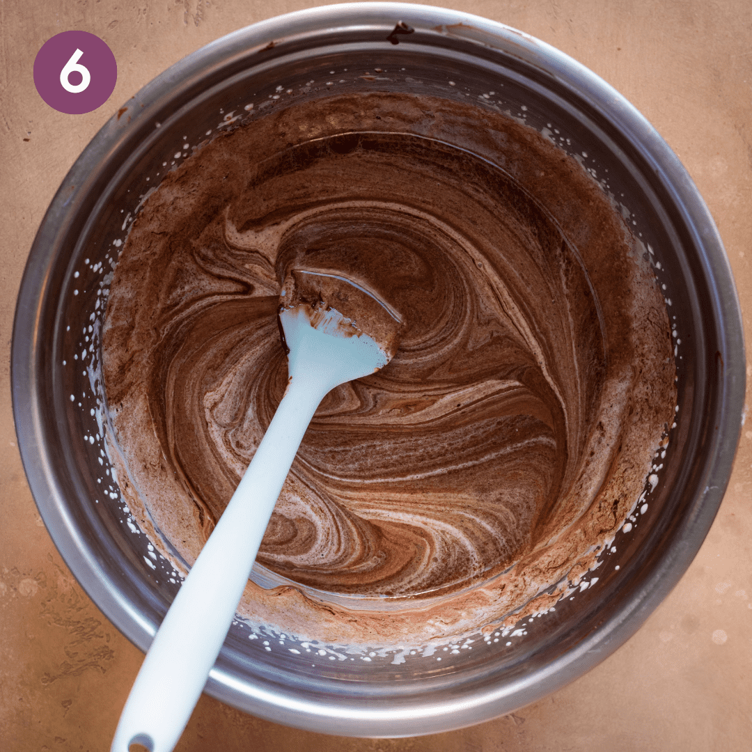 a silicone spatula in a bowl of wavy melted chocolate mixing into liquid ingredients for vegan brownie batter.