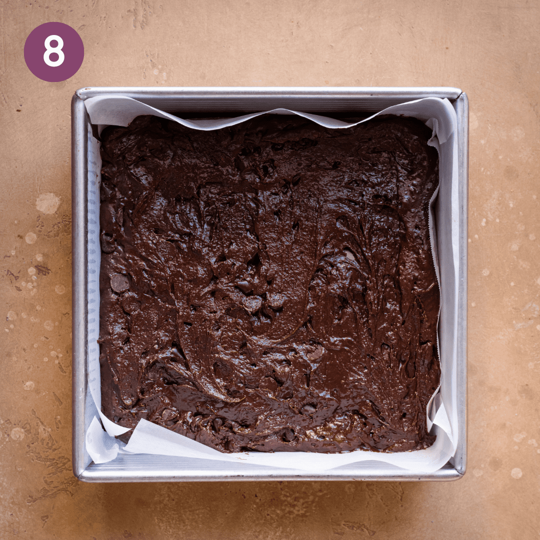 thick fudgy vegan brownie batter in a parchment paper lined square baking pan.