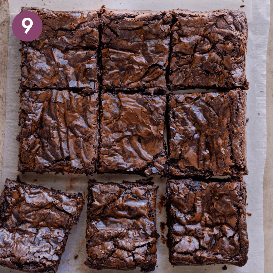 a grid of chewy vegan brownies sliced into 9 squares with a shiny top sitting on a parchment paper.