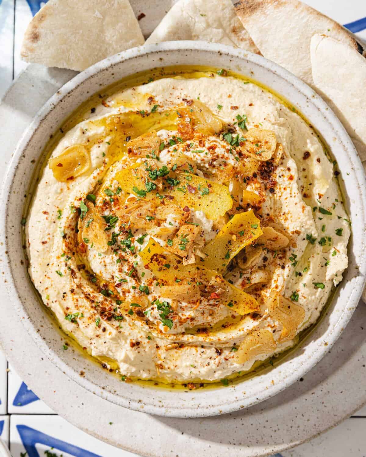 overhead view of hummus with lemon garlic topping in a bowl next to pita triangles.