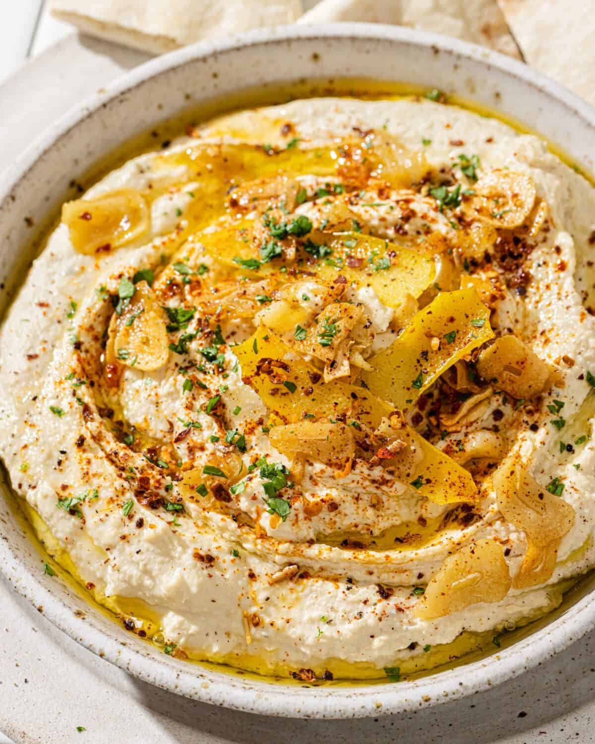 side view of a bowl of hummus with lemon garlic topping next to pita triangles.