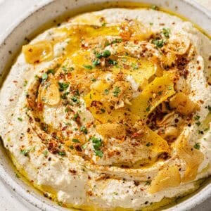 side view of a bowl of hummus with lemon garlic topping next to pita triangles.