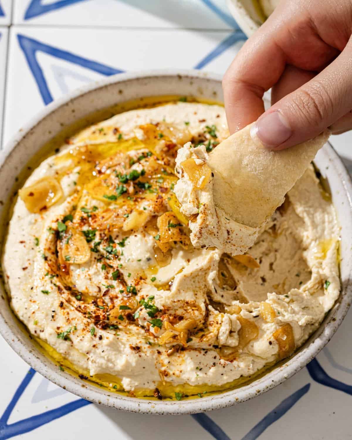 woman's hands dipping pita into a bowl of hummus.