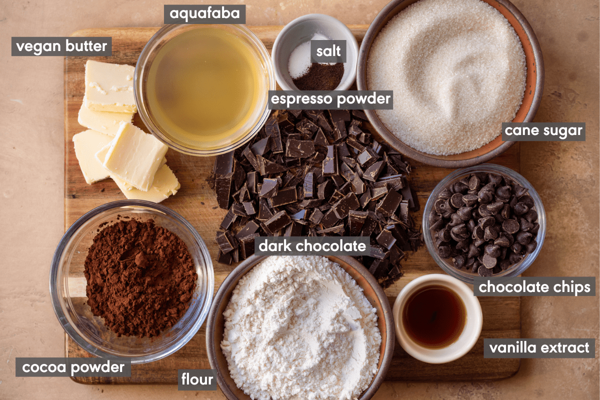 labeled ingredients for vegan brownies laid out on a wooden cutting board on a brown table.