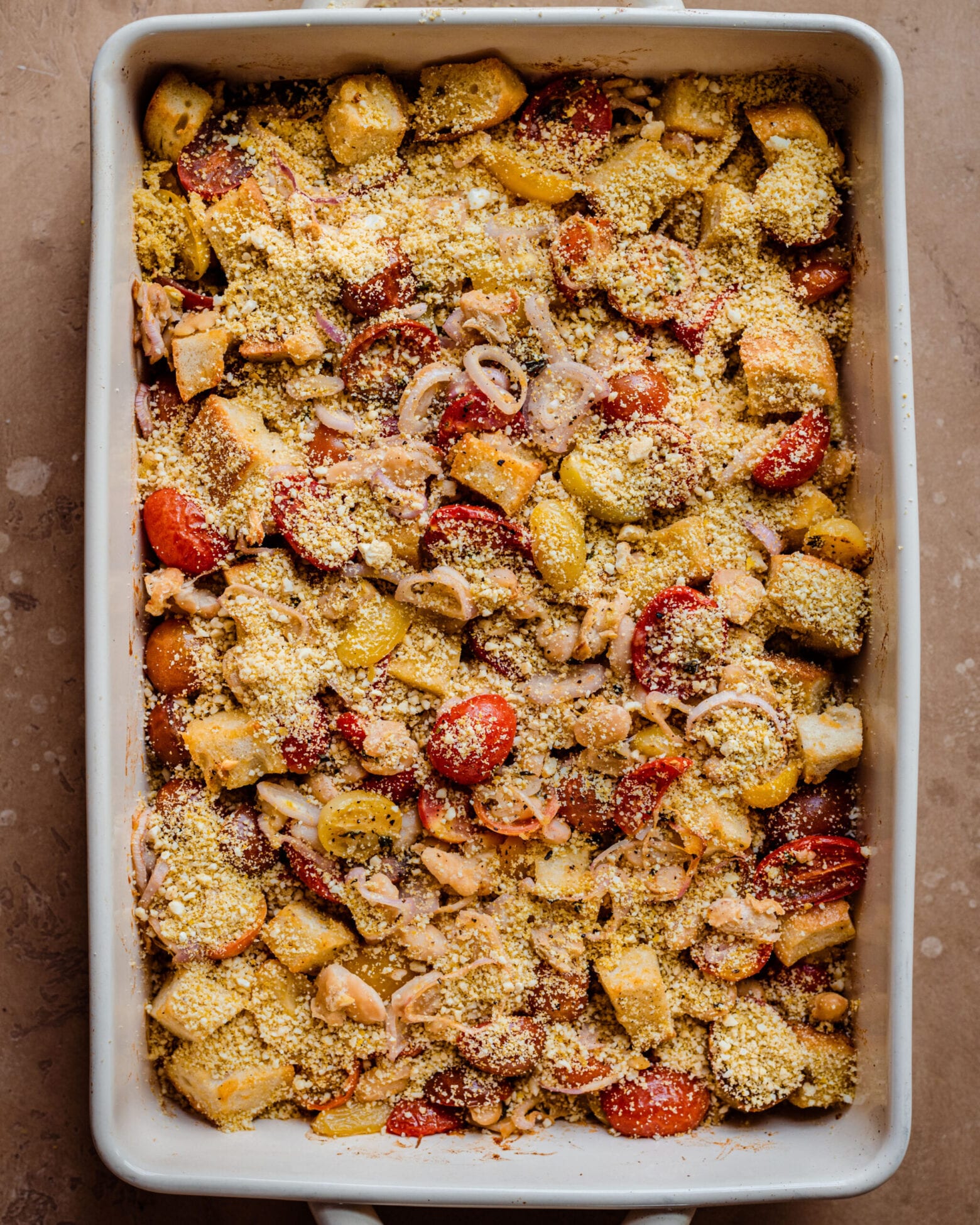 baked tomato casserole in baking pan with cashew parmesan on top.