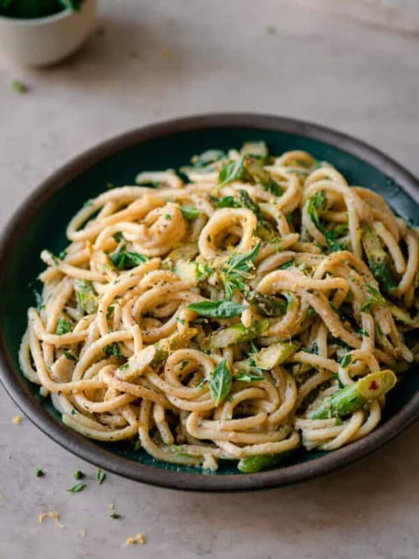shallow bowl of creamy lemon asparagus pasta on neutral backdrop.