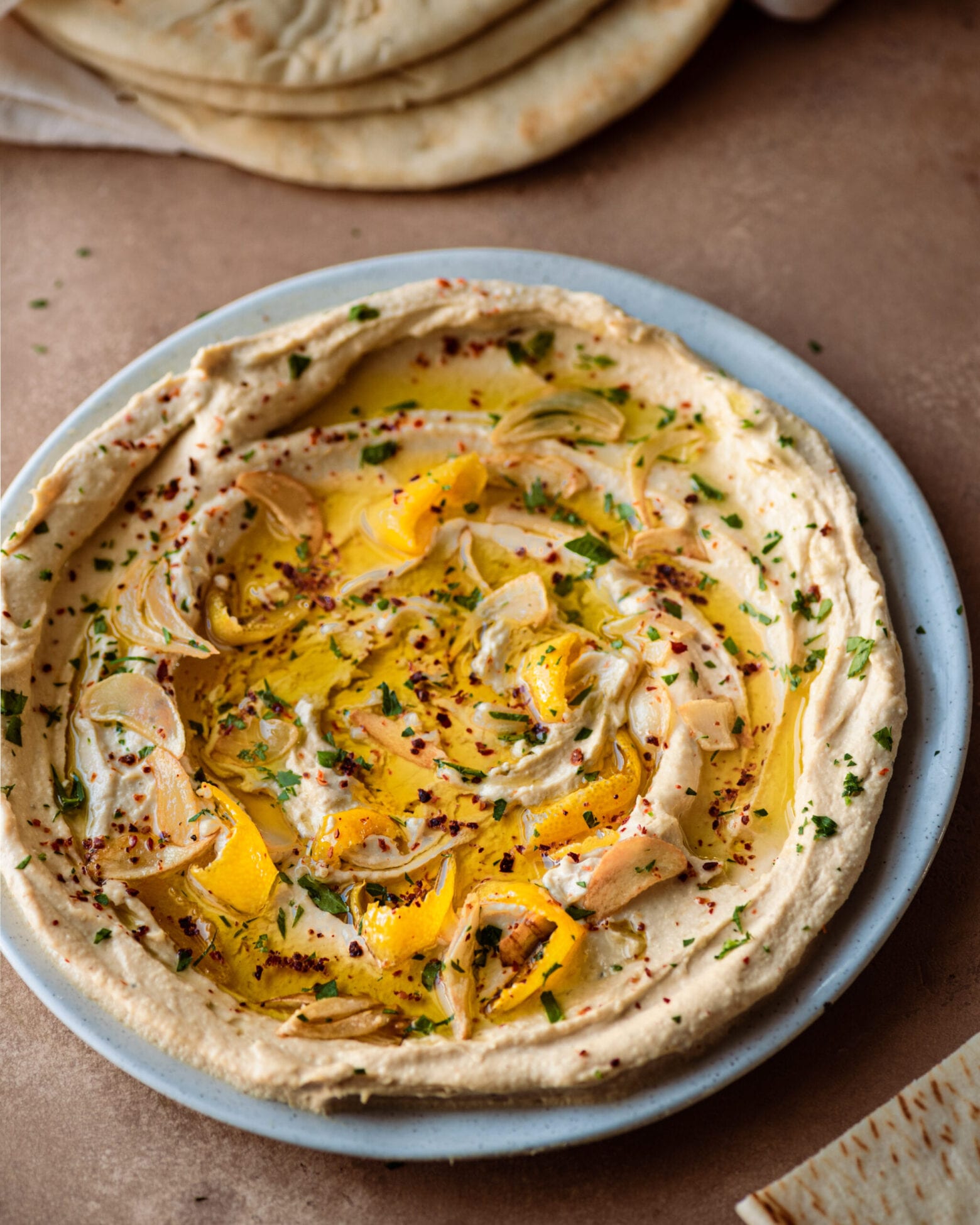 plate of creamy hummus with olive oil and herbs with pita bread