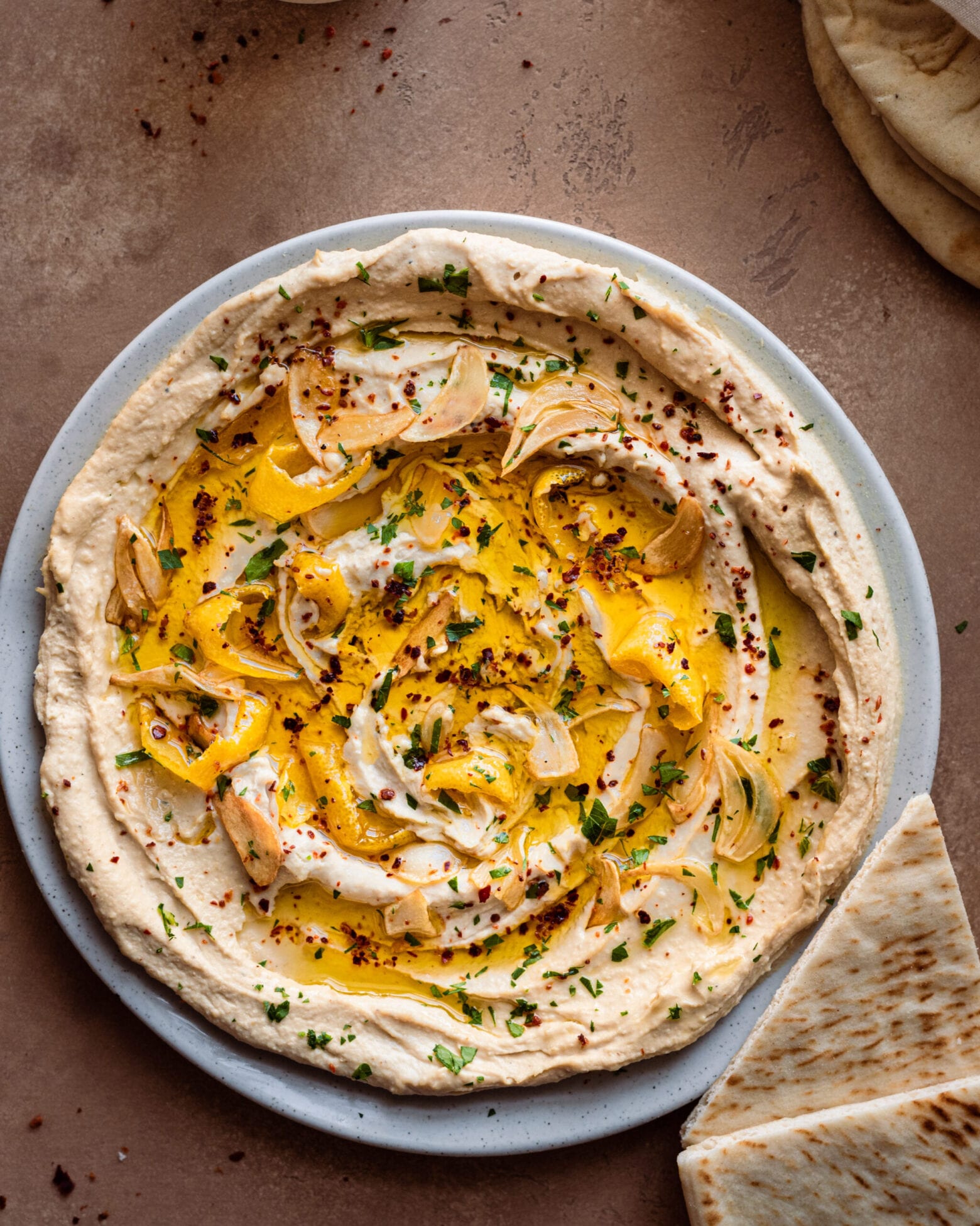 Hummus in a large shallow plate with garlic, lemon and olive oil on top.