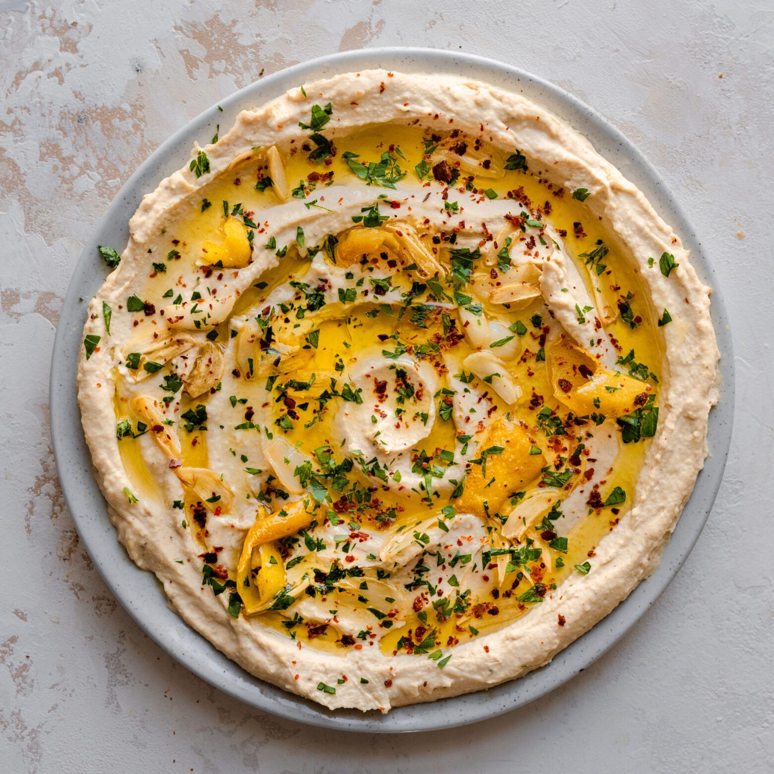 creamy hummus swirled on plate with olive oil, parsley, lemon, and paprika on top