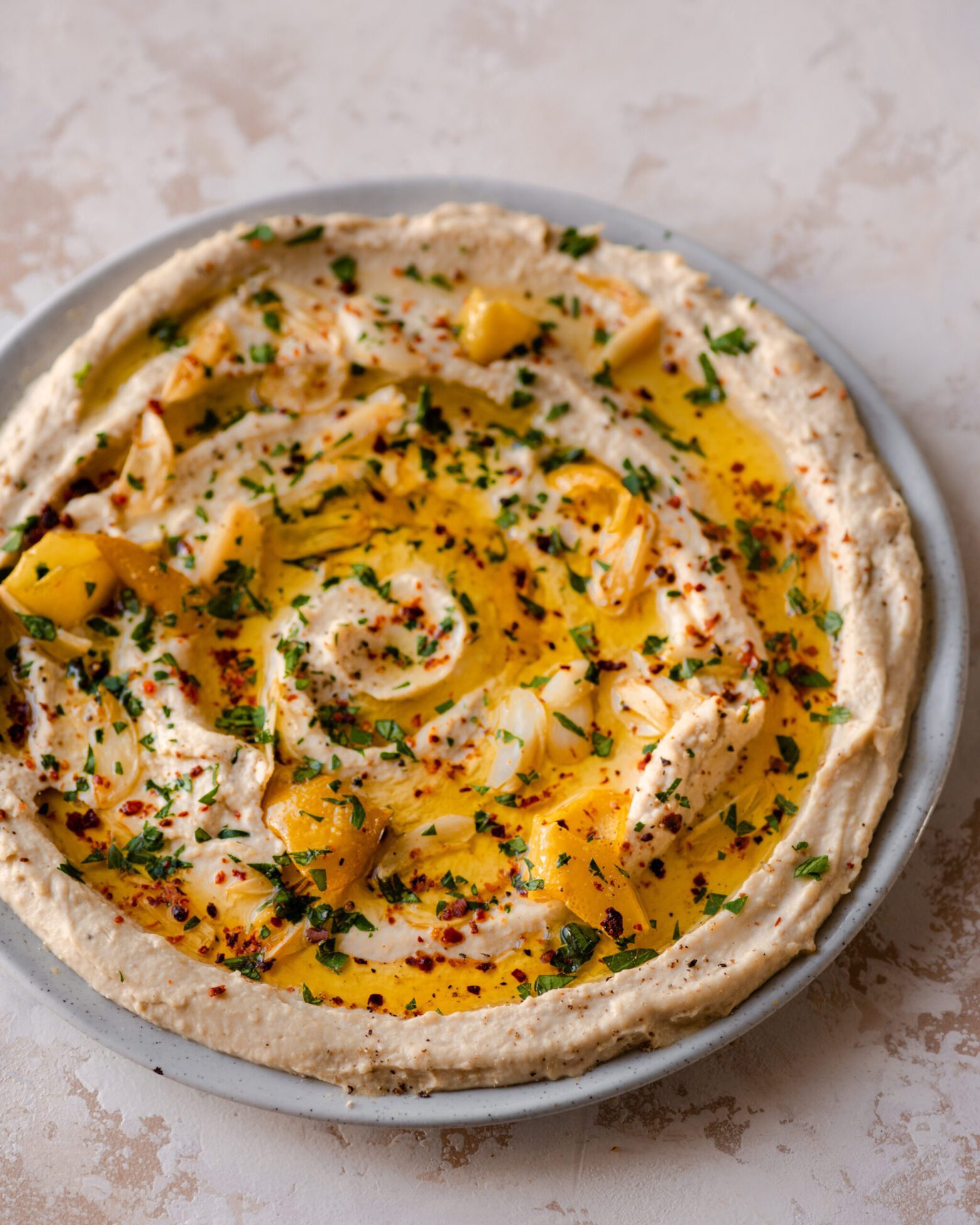 plate of smooth creamy hummus topped with olive oil and lemon on marble backdrop