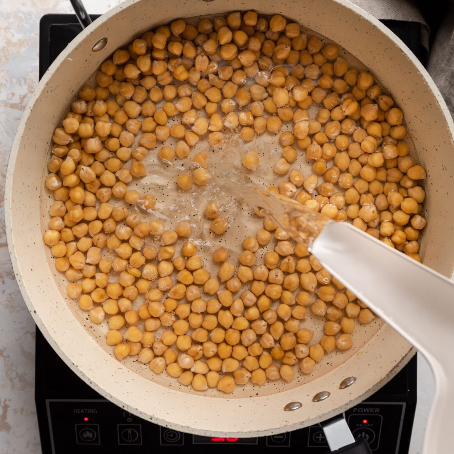pouring water into saucepan of chickpeas 