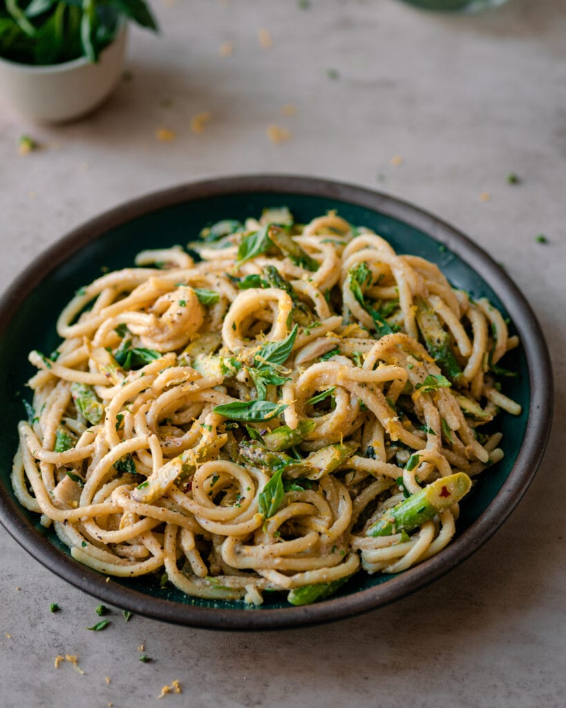 shallow bowl of creamy lemon asparagus pasta on neutral backdrop.