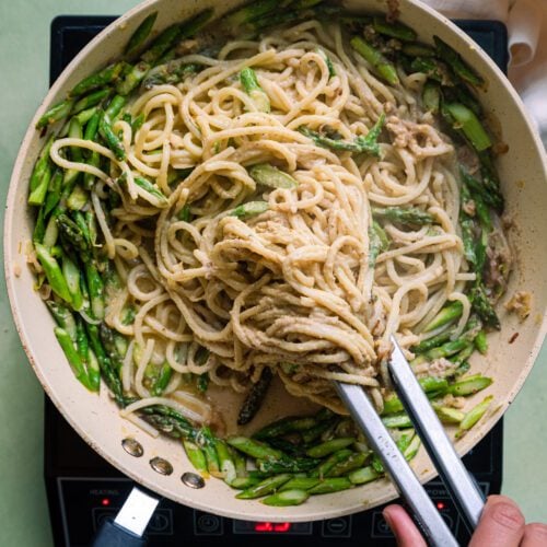 tossing spaghetti with tongs in a saute pan with asparagus