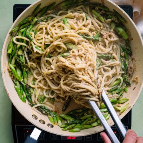 Tossing spaghetti with tongs in saute pan with asparagus