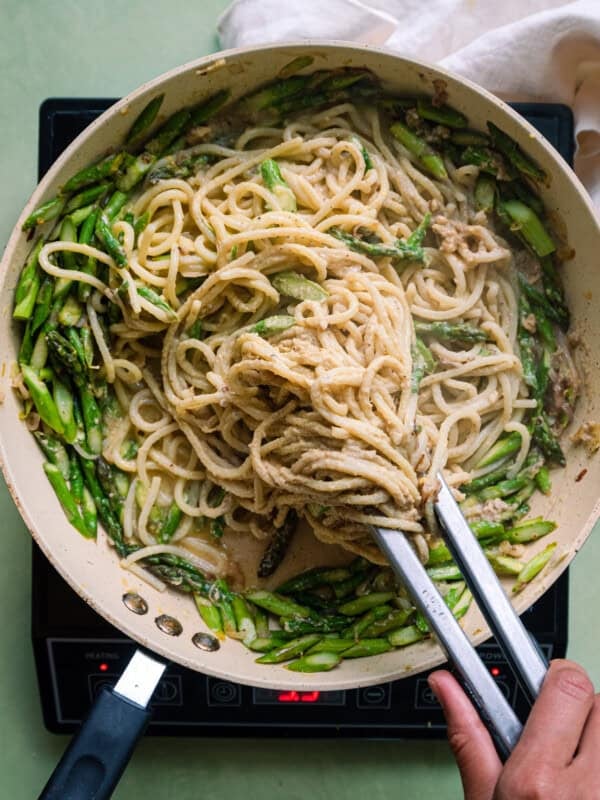 tossing spaghetti with tongs in a saute pan with asparagus