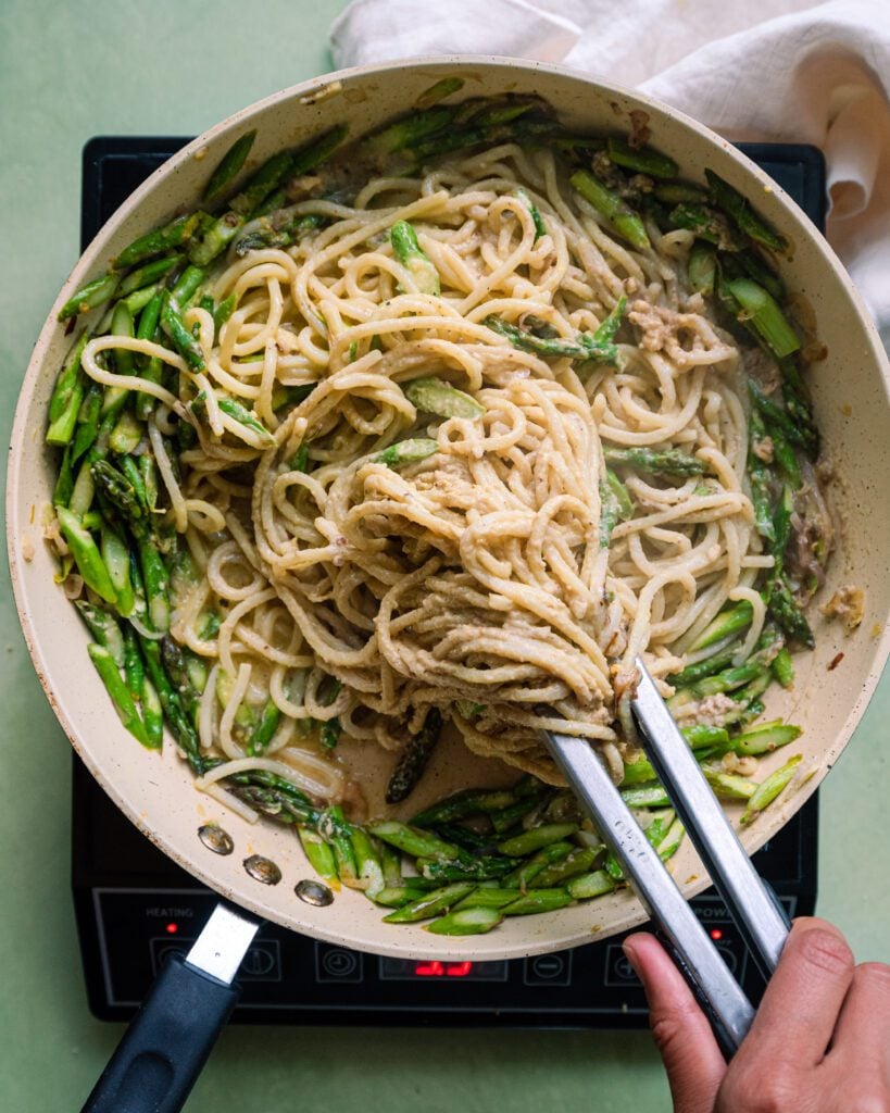 tossing spaghetti with tongs in a saute pan with asparagus