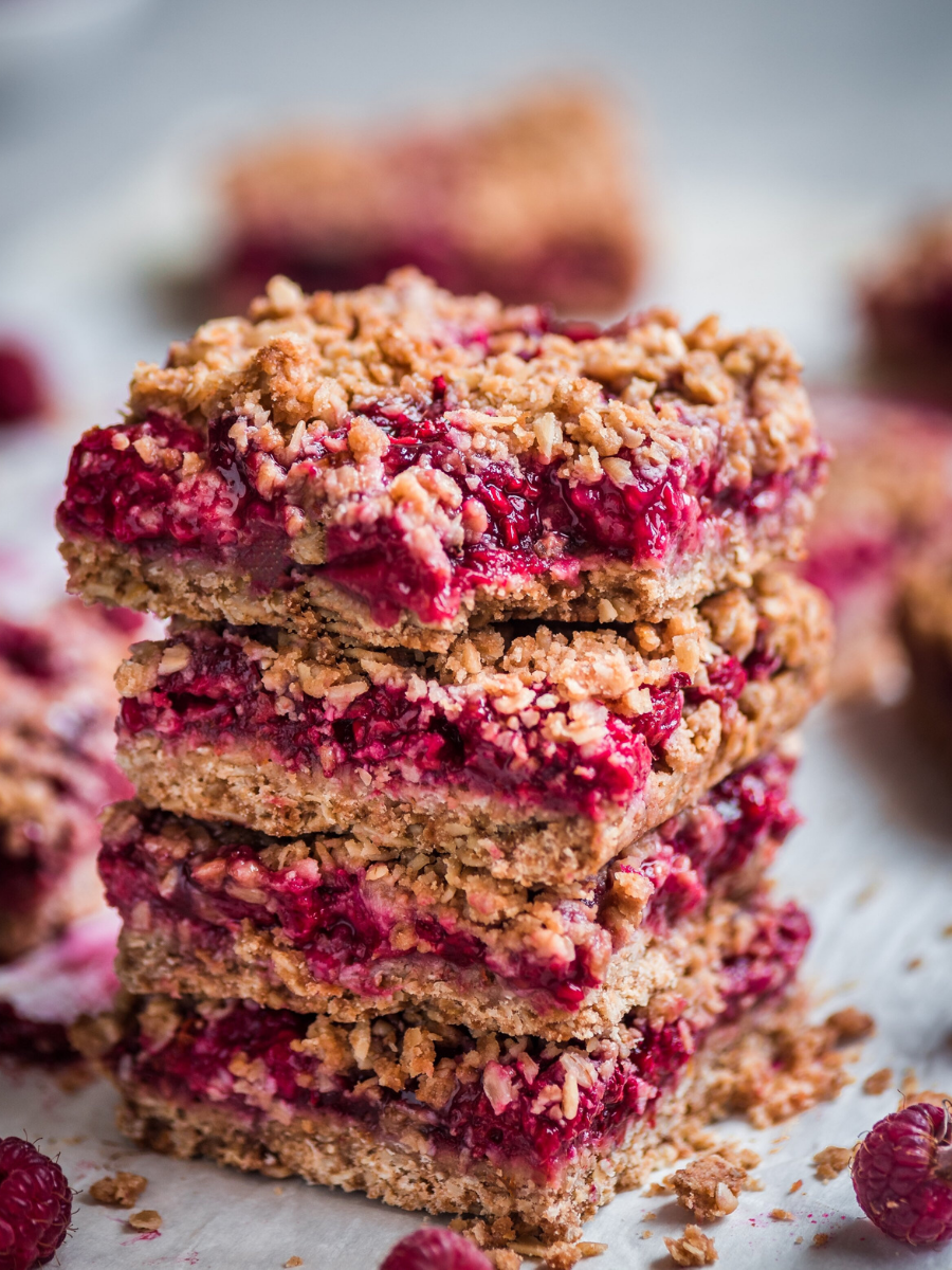 raspberry crumble bars stacked on top of each other on a piece of parchment paper.