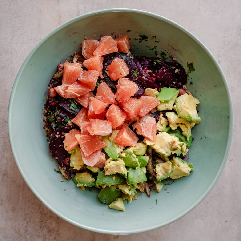 beet salad in large bowl with avocado and oranges on top