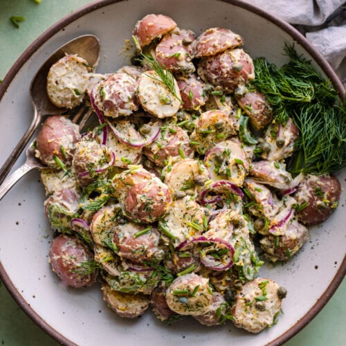 creamy vegan potato salad with dilll in a white bowl on a green backdrop