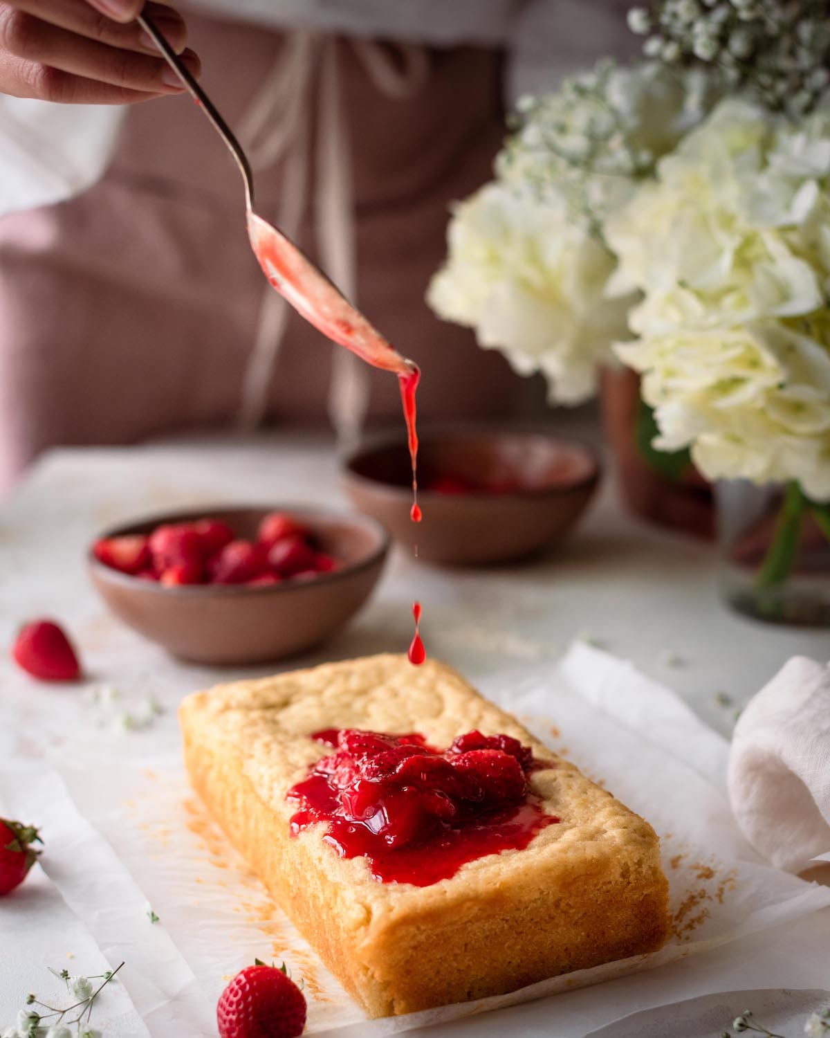 woman drizzling strawberry sauce onto lemon olive oil cake in romantic food photography scene