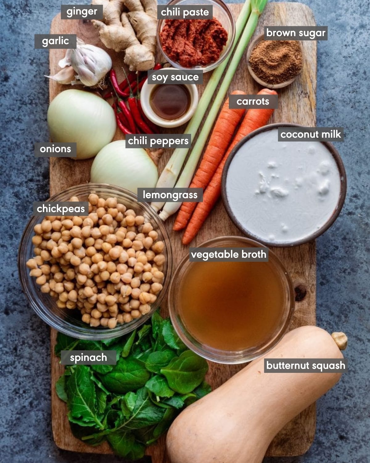 ingredients on cutting board with butternut squash, chickpeas, lemongrass, coconut milk, soy sauce, bird's eye chili peppers, spinach, soy sauce, brown sugar, chili paste, vegetable broth, coconut milk, garlic, ginger, and onions
