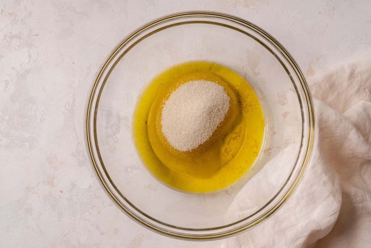 olive oil and sugar in mixing bowl on marble surface
